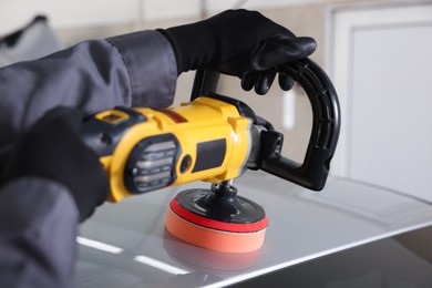 Photo of Man polishing car with orbital polisher indoors, closeup