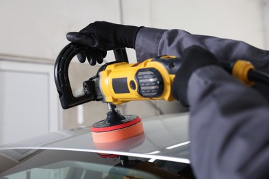 Photo of Man polishing car with orbital polisher indoors, closeup