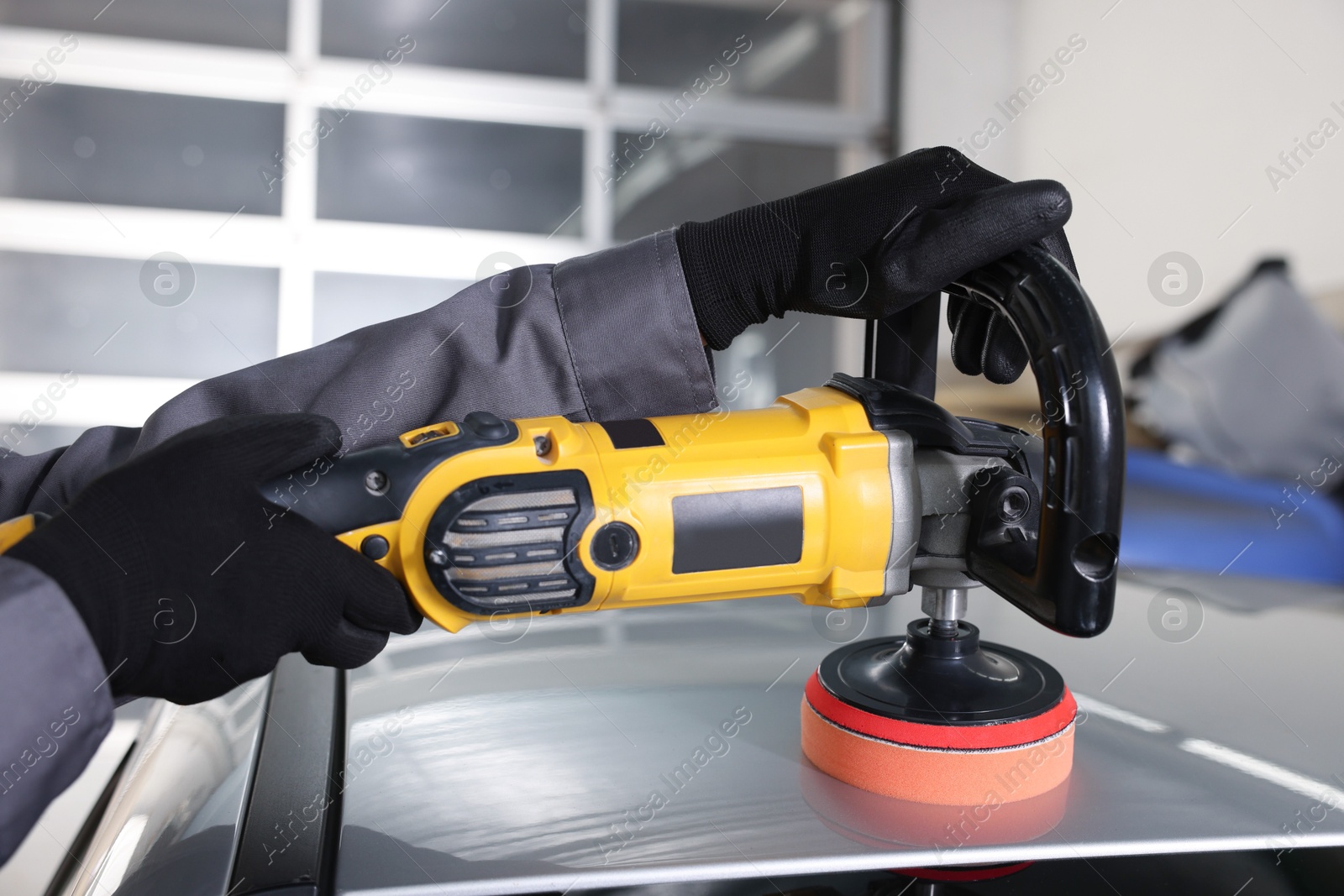 Photo of Man polishing car with orbital polisher indoors, closeup