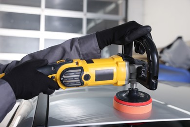 Photo of Man polishing car with orbital polisher indoors, closeup