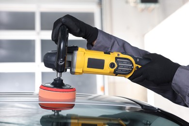 Photo of Man polishing car with orbital polisher indoors, closeup