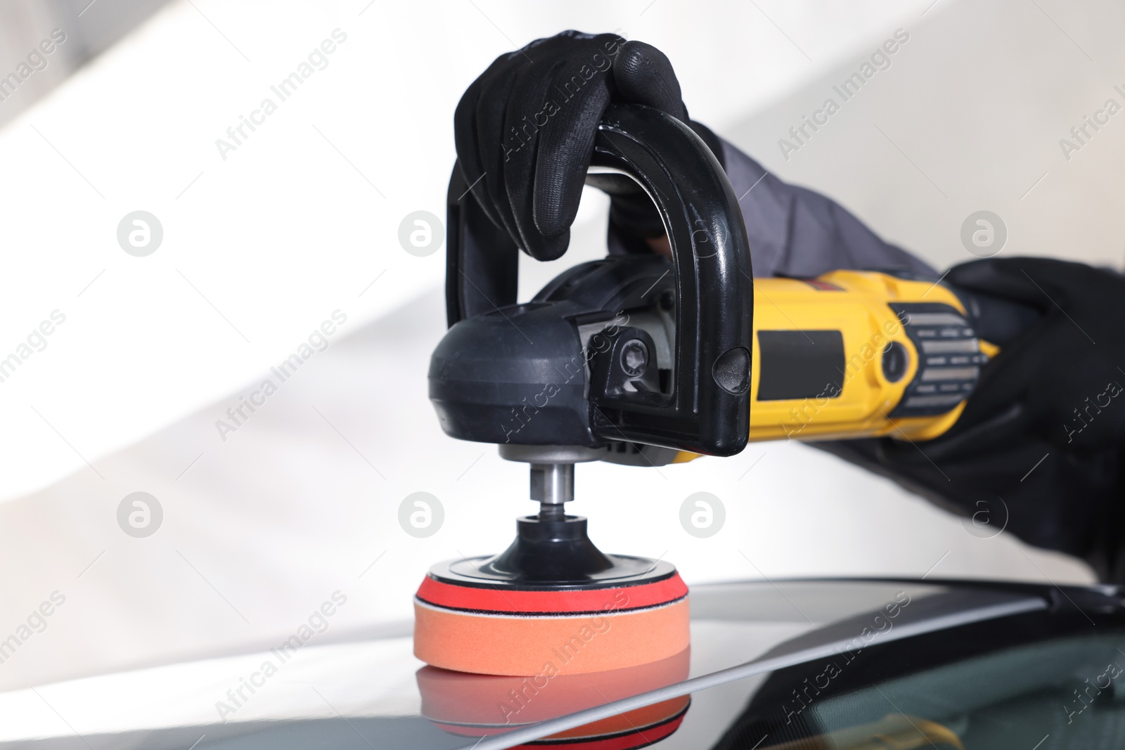 Photo of Man polishing car with orbital polisher indoors, closeup