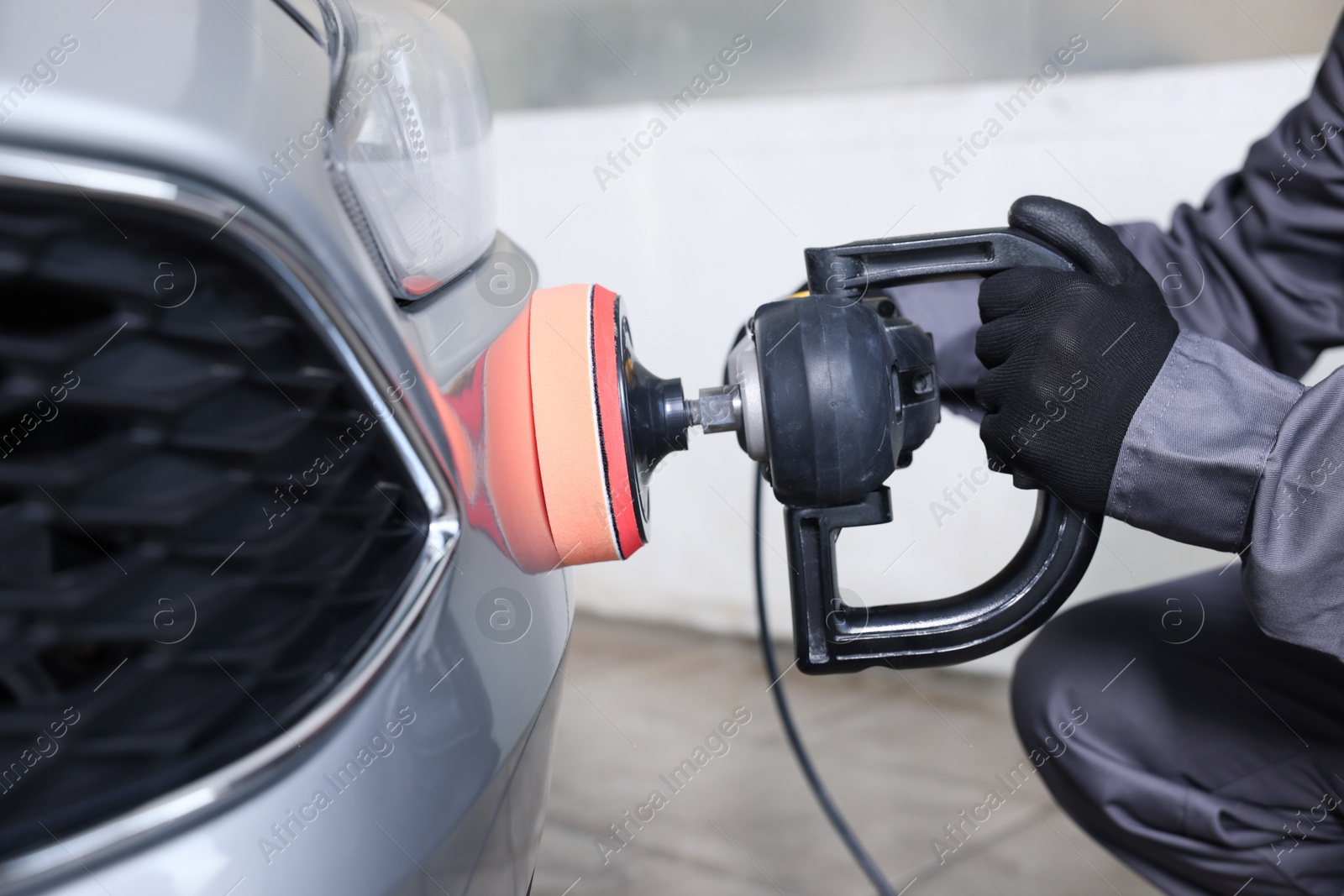 Photo of Man polishing car with orbital polisher indoors, closeup