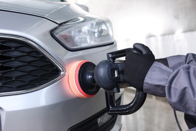 Photo of Man polishing car with orbital polisher indoors, closeup