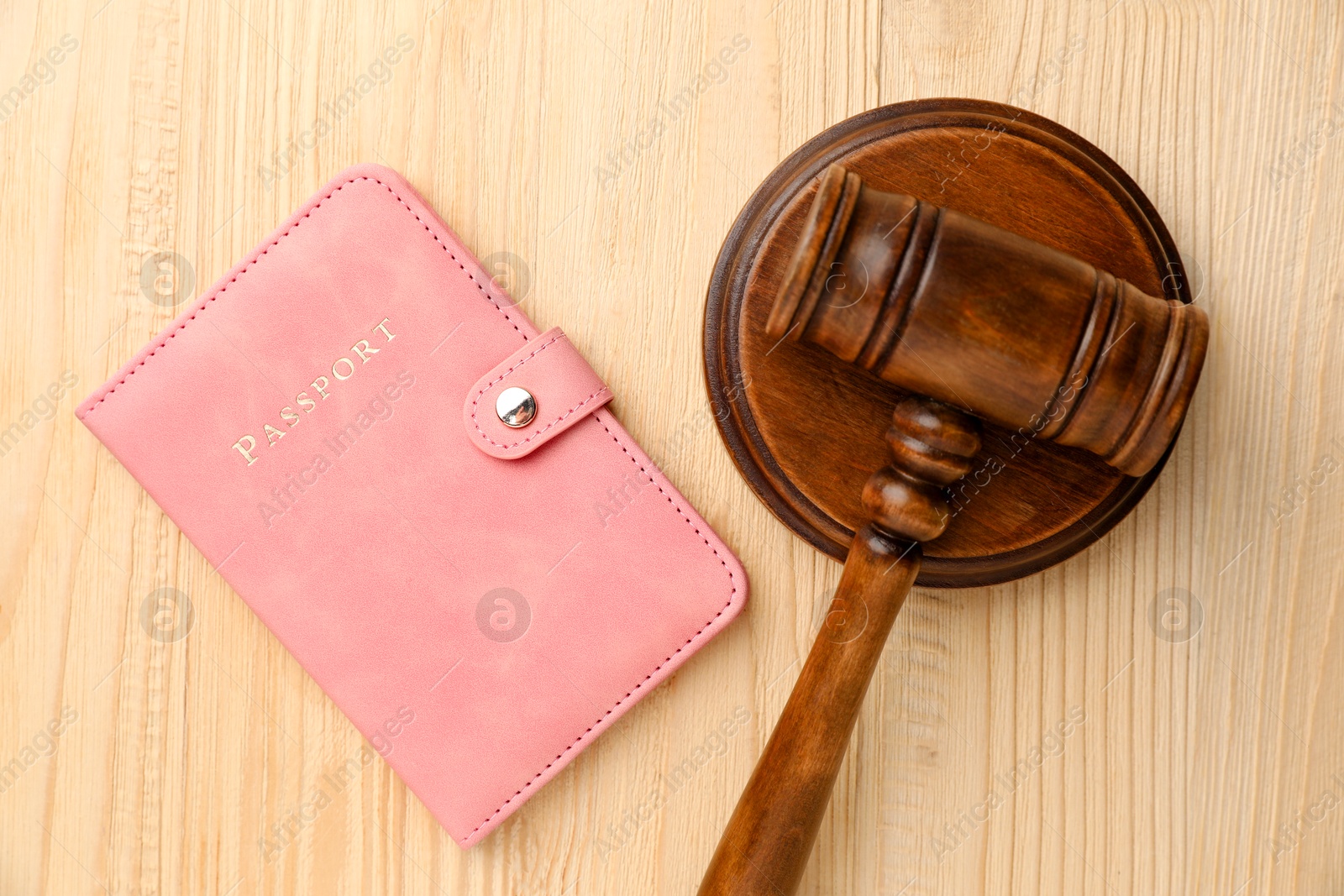 Photo of Passport in pink cover and judge's gavel on wooden table, top view