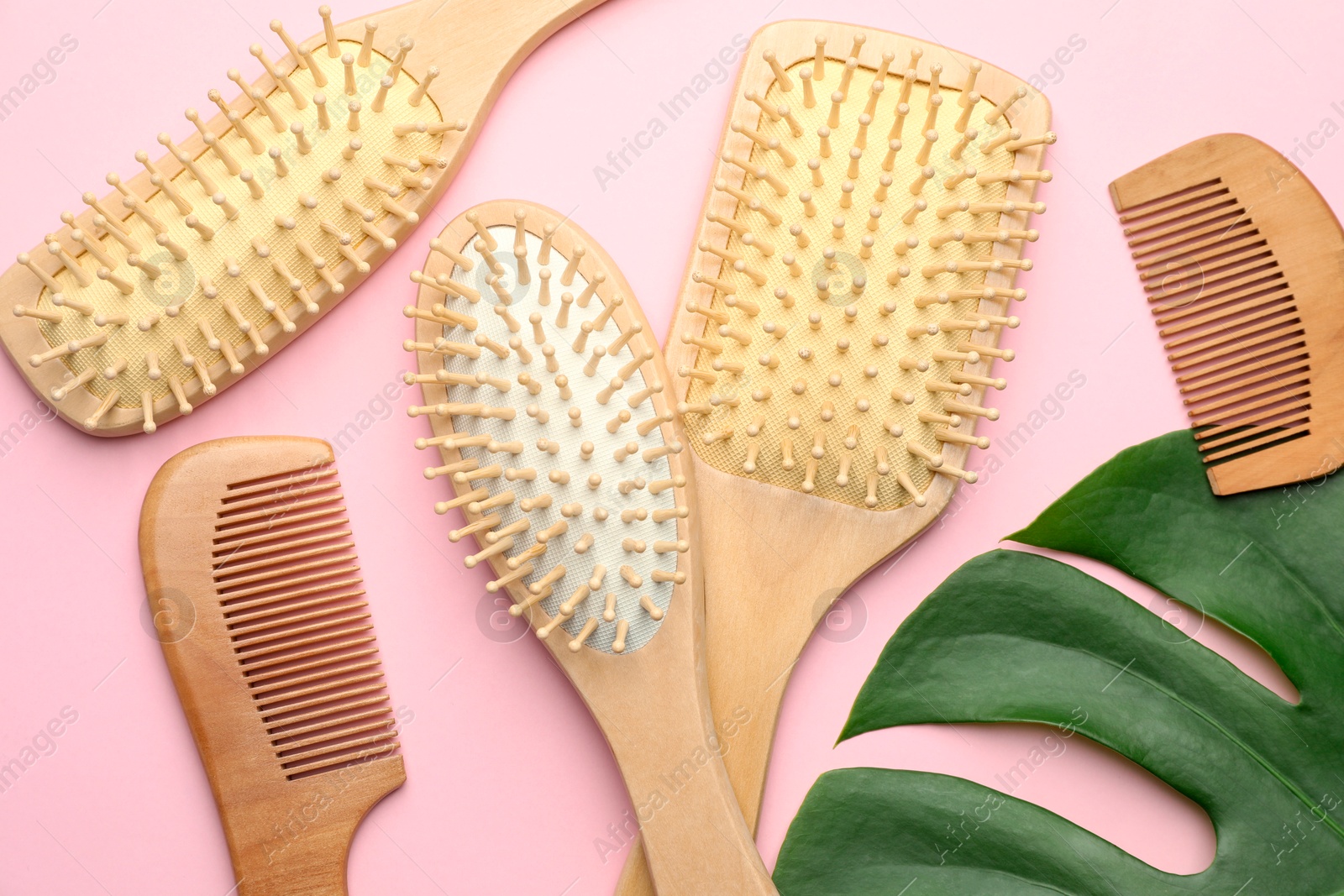 Photo of Wooden hair brushes, combs and monstera leaf on pink background, flat lay