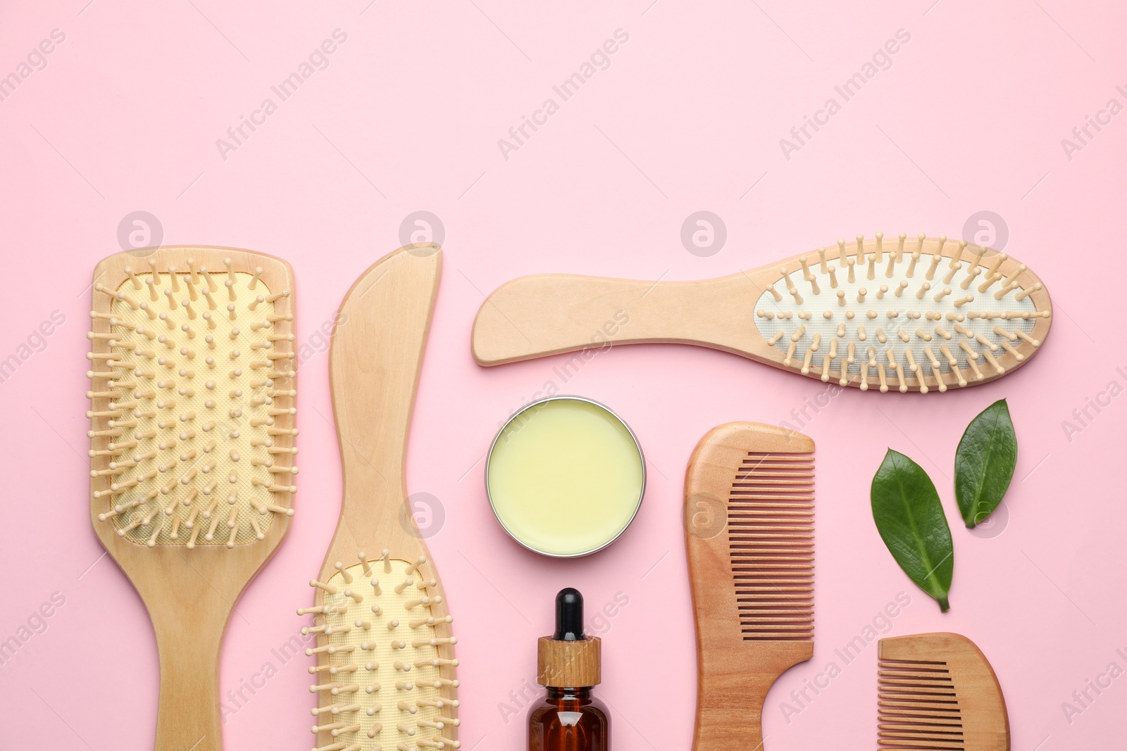 Photo of Wooden hair brushes, combs, cosmetic products and green leaves on pink background, flat lay