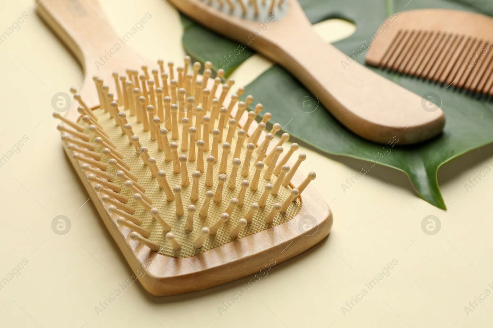 Photo of Wooden hair brushes, comb and monstera leaf on beige background, closeup