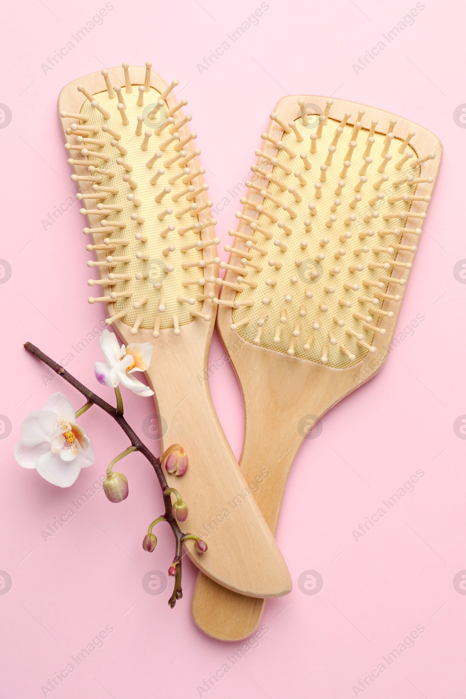 Photo of Wooden hair brushes and orchid branch on pink background, flat lay