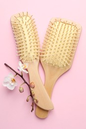 Photo of Wooden hair brushes and orchid branch on pink background, flat lay