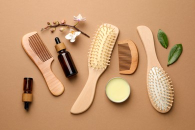 Photo of Wooden hair brushes, combs, cosmetic products and orchid branch on dark beige background, flat lay