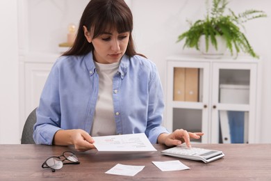 Photo of Paying bills. Woman with different invoices and calculator at wooden table indoors