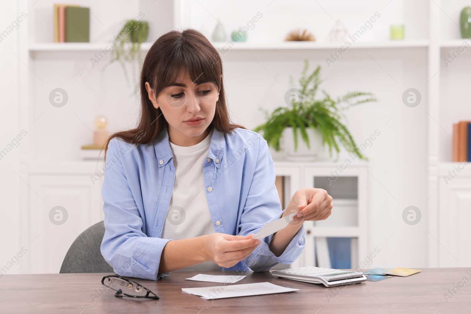 Photo of Paying bills. Woman with different invoices and calculator at wooden table indoors