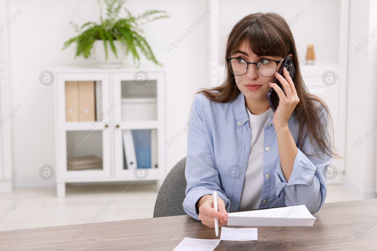 Photo of Paying bills. Woman with different invoices talking on phone at wooden table indoors, space for text