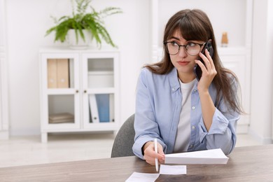 Photo of Paying bills. Woman with different invoices talking on phone at wooden table indoors, space for text