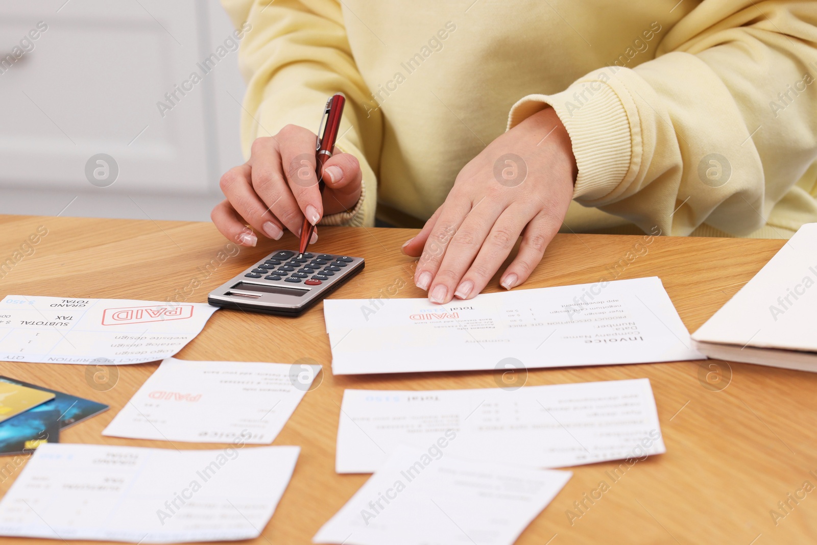 Photo of Paying bills. Woman with different invoices and calculator at wooden table indoors, closeup