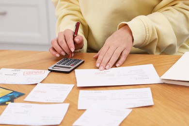 Photo of Paying bills. Woman with different invoices and calculator at wooden table indoors, closeup