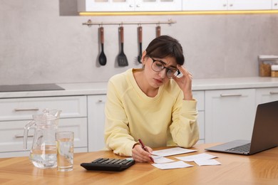 Photo of Paying bills. Upset woman with different invoices and calculator at wooden table indoors