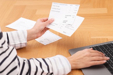 Photo of Paying bills. Woman with different invoices and laptop at wooden table indoors, closeup