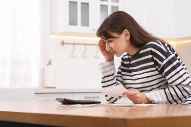 Photo of Paying bills. Woman with different invoices and calculator at wooden table indoors, space for text