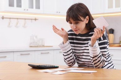 Photo of Paying bills. Upset woman with different invoices and calculator at wooden table indoors