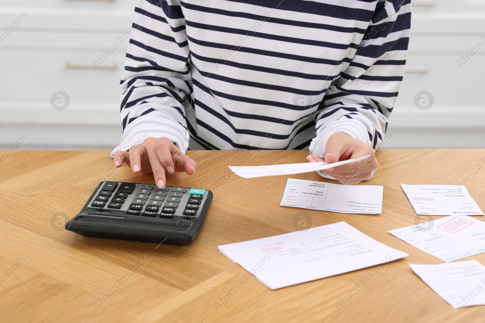 Photo of Paying bills. Woman with different invoices and calculator at wooden table indoors, closeup