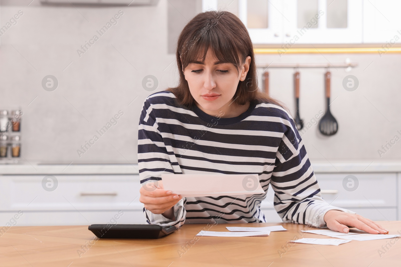 Photo of Paying bills. Woman with different invoices and calculator at wooden table indoors