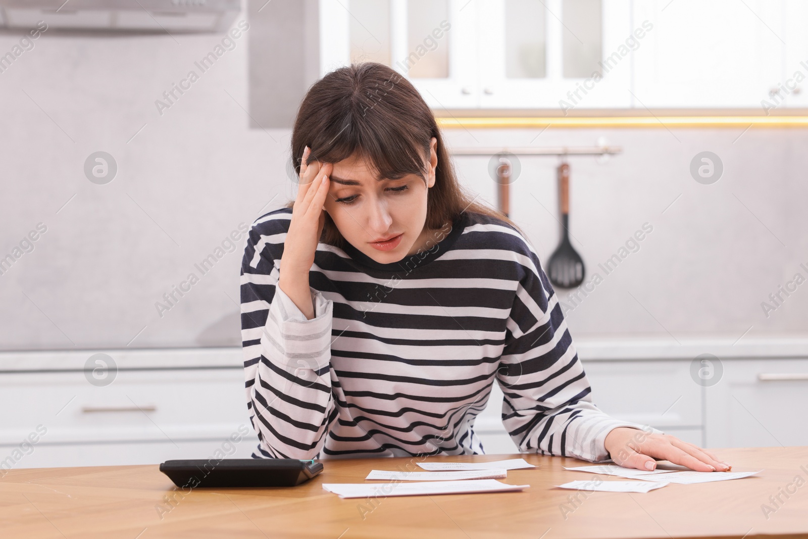 Photo of Paying bills. Upset woman with different invoices and calculator at wooden table indoors