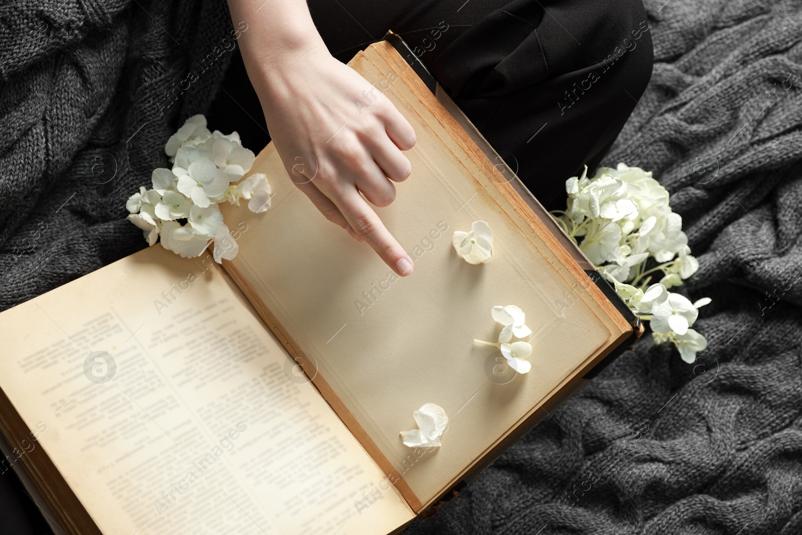 Photo of Woman reading book with beautiful flowers on blanket, top view