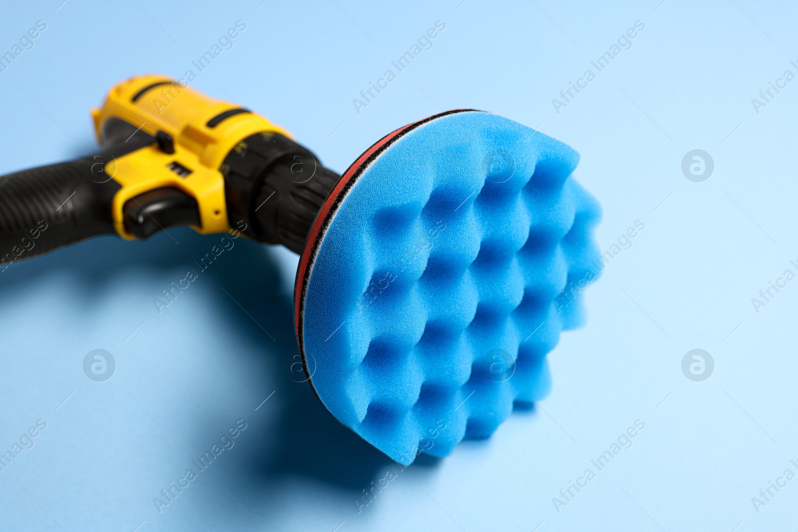 Photo of Electric screwdriver with polish pad on light blue background, closeup