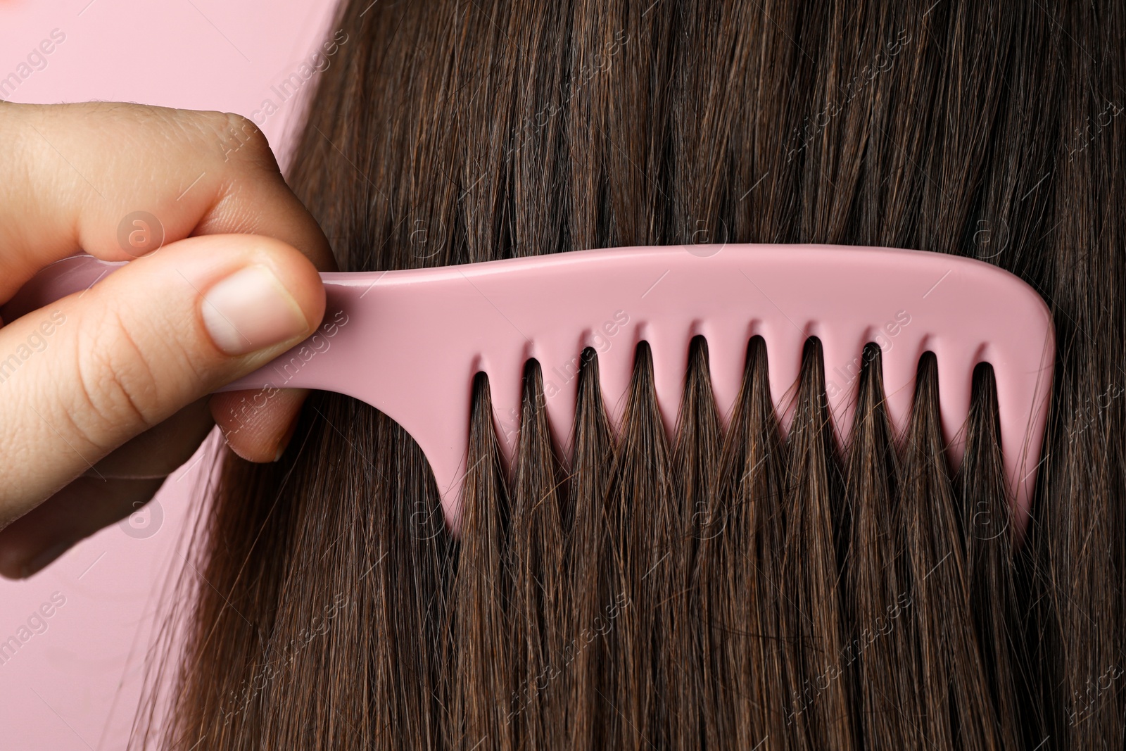 Photo of Woman brushing hair with plastic comb on pink background, closeup