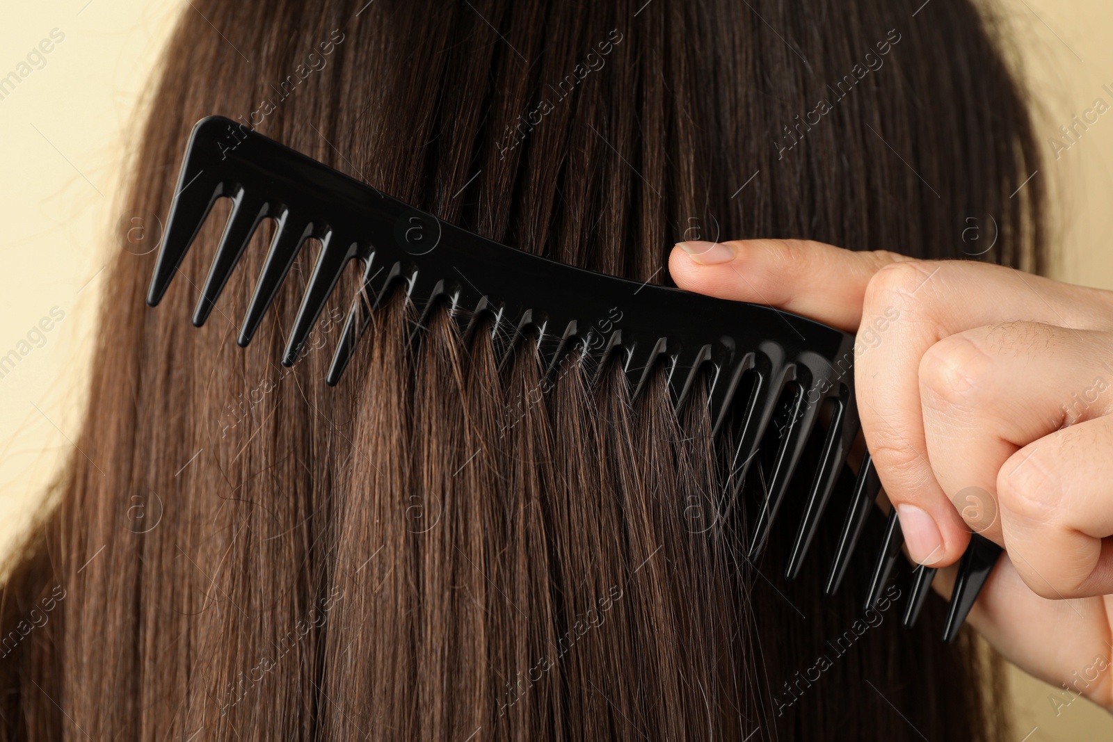 Photo of Woman brushing hair with plastic comb on beige background, closeup