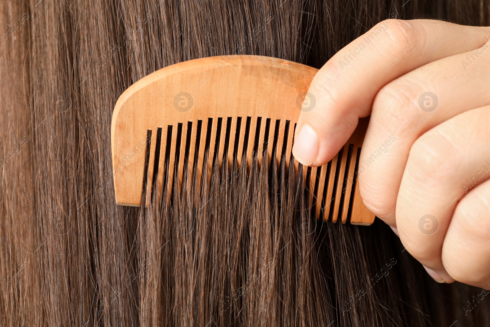 Photo of Woman brushing hair with wooden comb, closeup