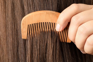 Photo of Woman brushing hair with wooden comb, closeup