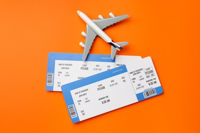 Photo of Travel agency. Flight tickets and plane model on orange background, flat lay