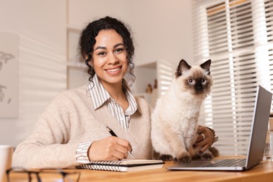 Photo of Beautiful woman with her cute cat working on laptop at desk in home office