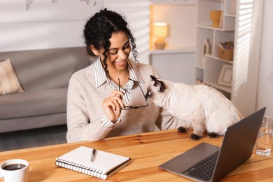 Photo of Beautiful woman with her cute cat working on laptop at desk in home office