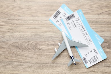 Photo of Travel agency. Flight tickets and plane model on wooden table, flat lay. Space for text