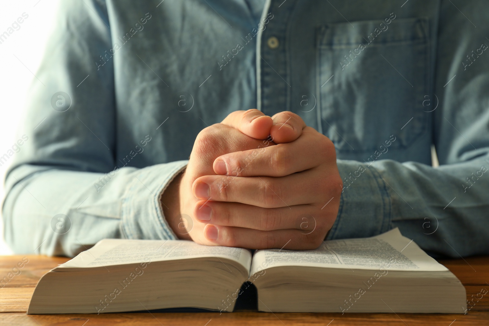 Photo of Man with open Holy Bible praying at wooden table, closeup