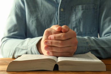 Photo of Man with open Holy Bible praying at wooden table, closeup