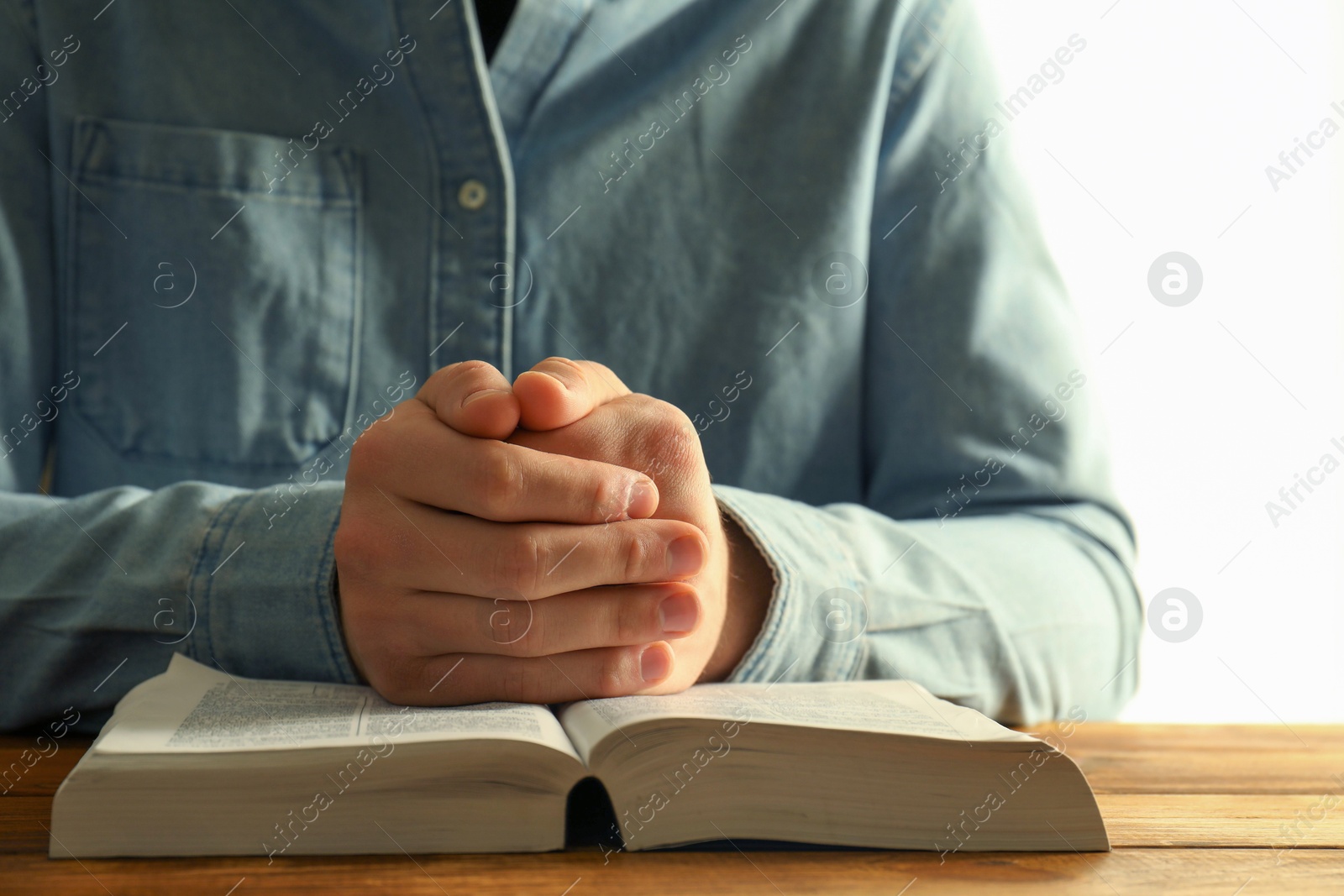 Photo of Man with open Holy Bible praying at wooden table, closeup