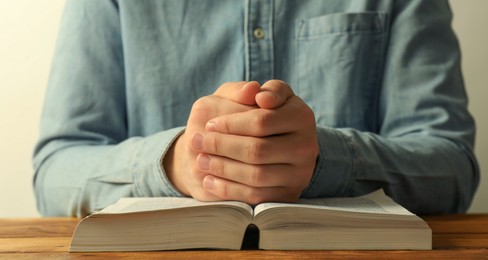 Photo of Man with open Holy Bible praying at wooden table, closeup