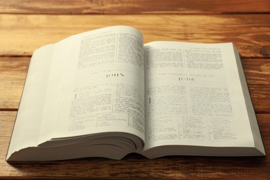 Photo of Open Holy Bible in English language on wooden table, closeup