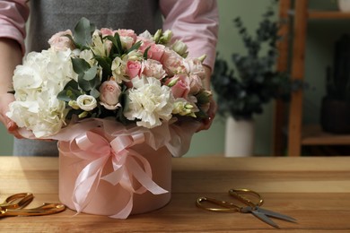 Photo of Florist with beautiful bouquet in box at table indoors, closeup