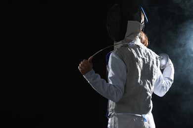 Photo of Fencer with epee in smoke on black background, space for text