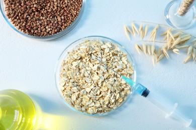 Photo of GMO concept. Petri dishes with cereal grains, florets and syringe on white table, flat lay