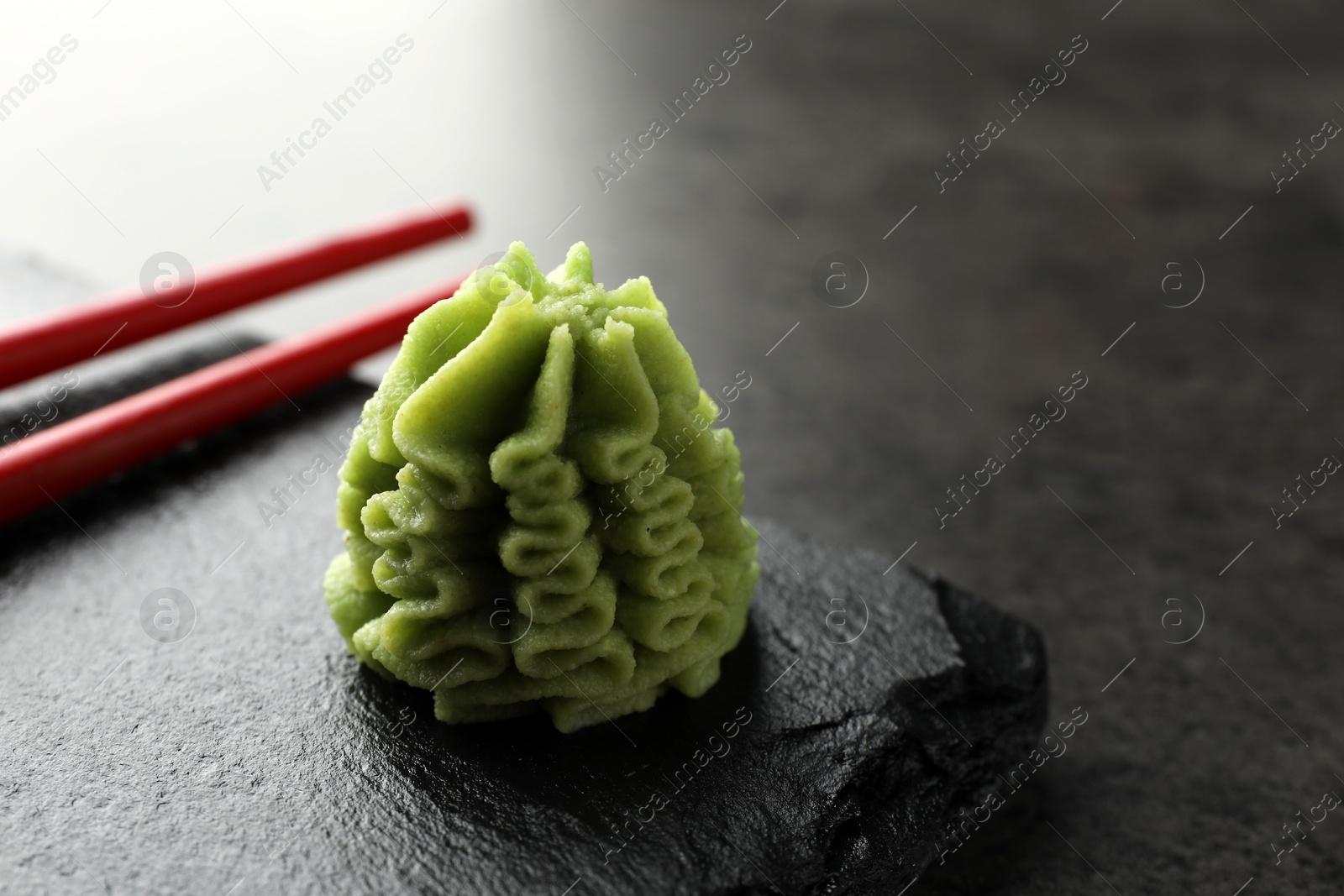 Photo of Hot wasabi paste and chopsticks on grey table, closeup