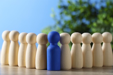 Photo of Human resources concept. Blue figure among wooden ones on table against blurred background, closeup. Space for text