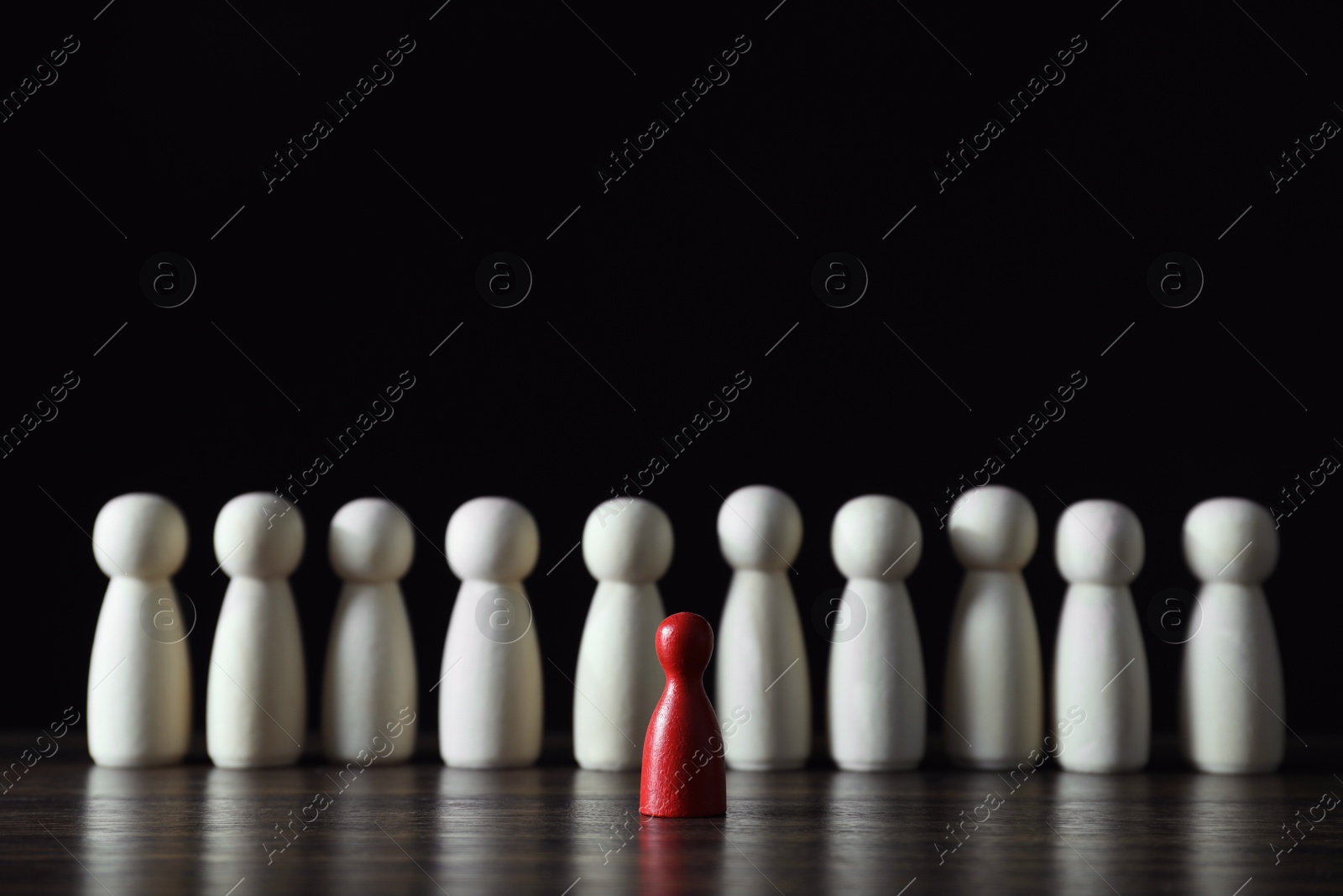 Photo of Human resources concept. Red figure in front of wooden ones on table against dark background, closeup. Space for text