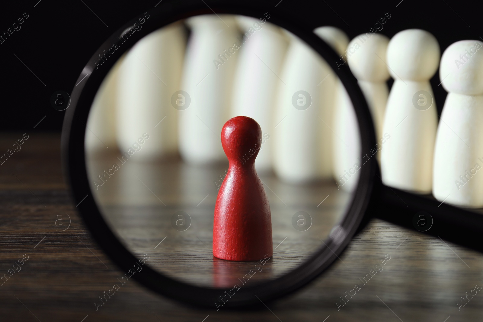 Photo of Human resources concept. Looking at red figure through magnifying glass on table against dark background, closeup